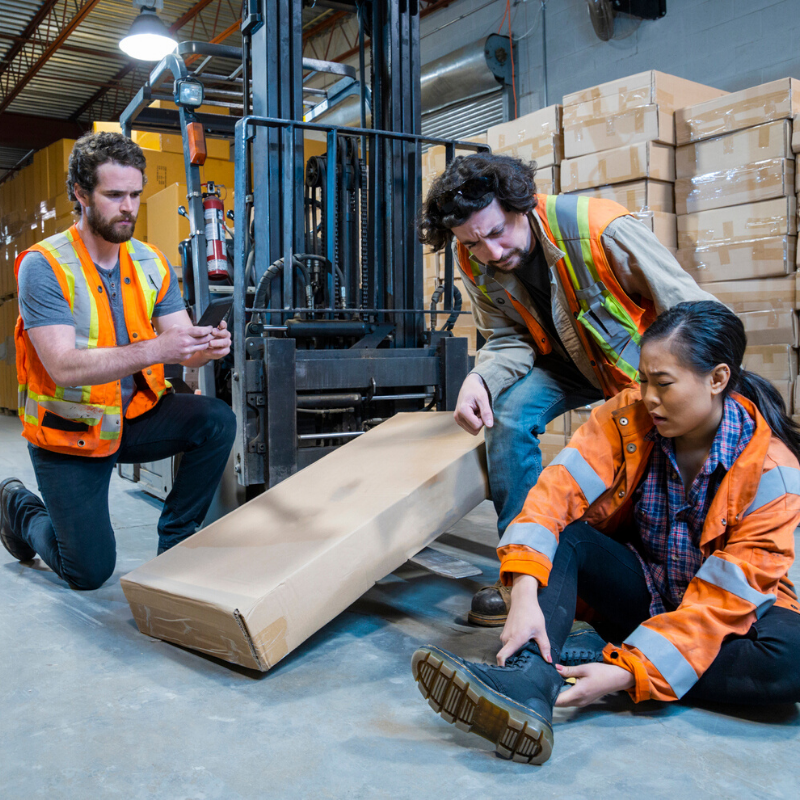 Three warehouse workers around a forklift truck with one holding their ankle